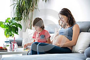 Young pregnant woman, reading a book at home to her boy