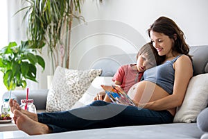 Young pregnant woman, reading a book at home to her boy
