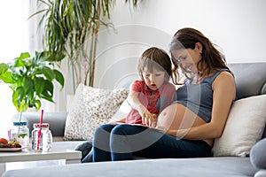 Young pregnant woman, reading a book at home to her boy