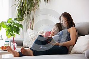 Young pregnant woman, reading a book at home to her boy