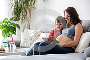 Young pregnant woman, reading a book at home to her boy