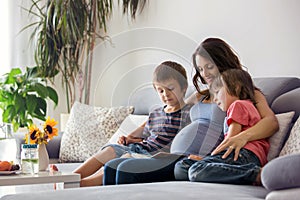 Young pregnant woman, reading a book at home to her two boys