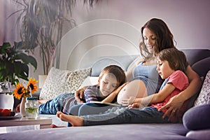 Young pregnant woman, reading a book at home to her two boys