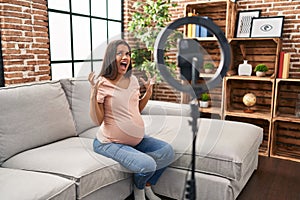 Young pregnant woman recording vlog tutorial with smartphone at home crazy and mad shouting and yelling with aggressive expression