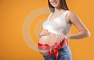 Young pregnant woman with red bow on belly against yellow background, closeup and space for text. Time to give birth