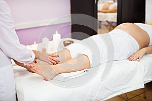 Young pregnant woman relaxing with hand leg massage at beauty sp