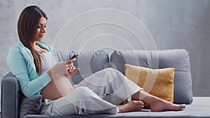 Young pregnant woman is resting at home with a snartphone and expecting a baby. The concept of pregnancy, motherhood