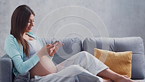 Young pregnant woman is resting at home with a snartphone and expecting a baby. The concept of pregnancy, motherhood