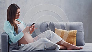 Young pregnant woman is resting at home with a snartphone and expecting a baby. The concept of pregnancy, motherhood