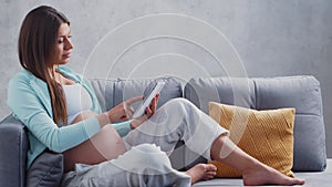 Young pregnant woman is resting at home with a tablet computer and expecting a baby. The concept of pregnancy