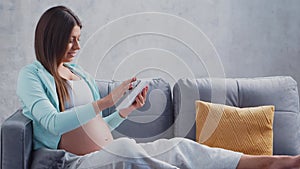 Young pregnant woman is resting at home with a tablet computer and expecting a baby. The concept of pregnancy