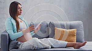 Young pregnant woman is resting at home with a tablet computer and expecting a baby. The concept of pregnancy