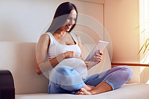 Young pregnant woman resting with tablet on sofa at home