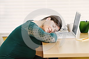 Young pregnant woman rests at her desk