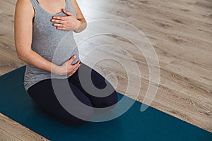 Young pregnant woman sat on mat doing prenatal yoga holding belly photo