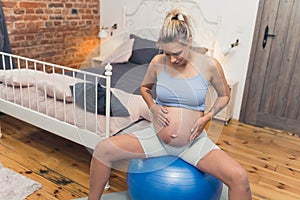 young pregnant woman sitting on a fit ball at home, pregnancy concept