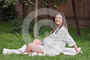Young pregnant woman is sitting in the garden on the grass