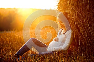 Young Pregnant Woman Sitting by the Haystack