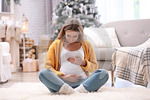 Young pregnant woman sitting in room decorated for Christmas