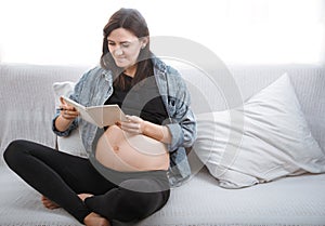 Young pregnant woman sitting on the sofa and reading a book