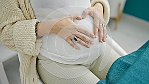 Young pregnant woman sitting on table doing heart symbol with hands on belly at dinning room