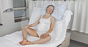 Young pregnant woman sitting upright on delivery bed photo