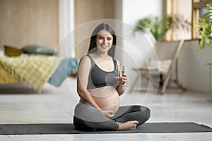 Young Pregnant Woman Sitting On Yoga Mat And Holding Glass With Water