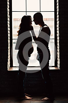 A young pregnant woman is standing with her husband near the window in the studio