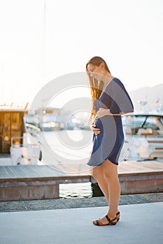 Young pregnant woman standing on the pier stroking her belly