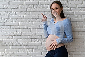 young pregnant woman. stands near a brick wall, pointing his index finger to an empty spot.