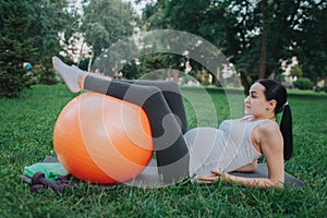 Young pregnant woman suffer from pain in hips area. She lying on yoga mate in park. Model hold hands on hips and legs on