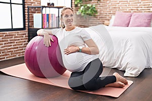 Young pregnant woman touching belly leaning on fit ball at bedroom