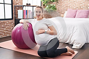 Young pregnant woman touching belly leaning on fit ball at bedroom