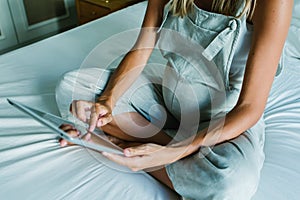 Young pregnant woman using a digital tablet while resting on bed at home