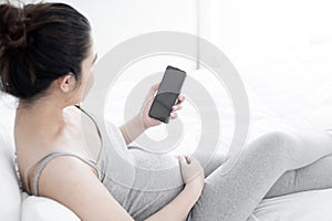 Young pregnant woman using smartphone with blank screen lying on bed.