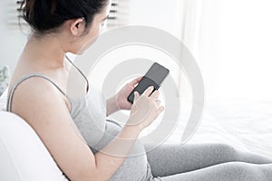 Young pregnant woman using smartphone with blank screen lying on bed.