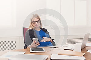 Young pregnant woman using smartphone at office