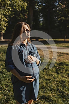 Young pregnant woman walking in park hugging belly