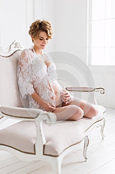 Young pregnant woman wearing lace dress in white interior. Fashion shot.