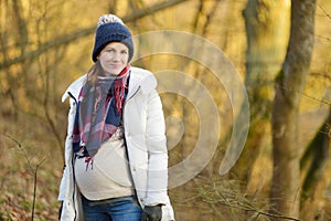 Young pregnant woman wearing warm jacket and beanie. Expecting mom having fun outdoors on a spring day photo