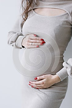 A young pregnant woman in a white dress, expecting a baby, hugs her stomach. Belly close-up, surrogacy.