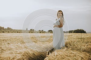 Young pregnant woman in white dress relaxing outside in nature