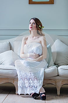 Young pregnant woman in white dress sitting