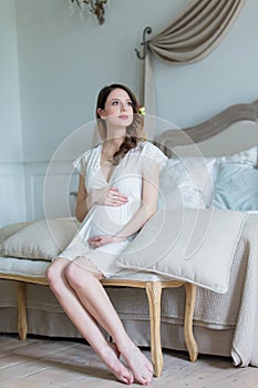 Young pregnant woman in white dress sitting
