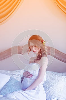 Young pregnant woman in white dress sitting