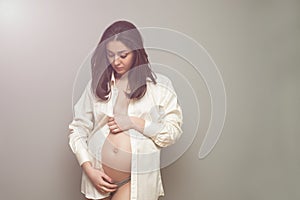 Young pregnant woman in white shirt holding her hands on belly