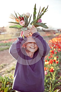 Young preteen girl stretching bunch of tulips to the camera, sunset outdoor scene.
