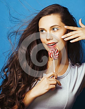 Young pretty adorable brunette woman with candy close up posing on blue background, like doll makeup, fashion beauty