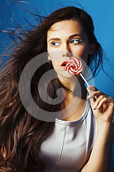 Young pretty adorable brunette woman with candy close up posing on blue background, like doll makeup, fashion beauty