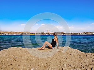 Young pretty adult girl sits on a rock and looks at the panorama of Sharm El Sheikh on the Red Sea. Caucasian woman on the